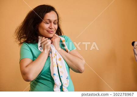 Beautiful Latin American pregnant woman hugging a cute baby jumpsuit, standing with her eyes closed over yellow background, expressing positive emotion, enjoying happy carefree pregnancy and maternity Beautiful Latin American pregnant woman hugging a cute baby jumpsuit, standing with her eyes closed over yellow background, expressing positive emotion, enjoying happy carefree pregnancy and maternity 102278967