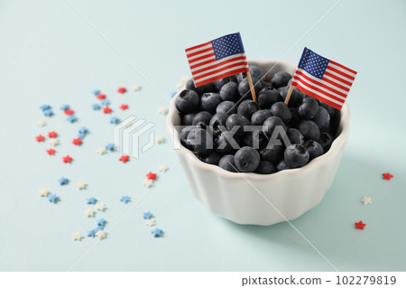 Blueberry decorated American flags in white bowl on blue background. Blueberry decorated American flags in white bowl on blue background. 102279819