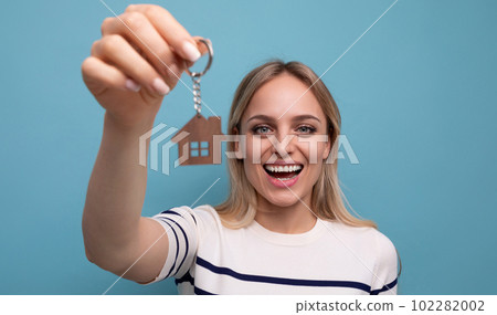 joyful happy young woman holding house key chain and rejoices buying real estate on blue isolated 102282002