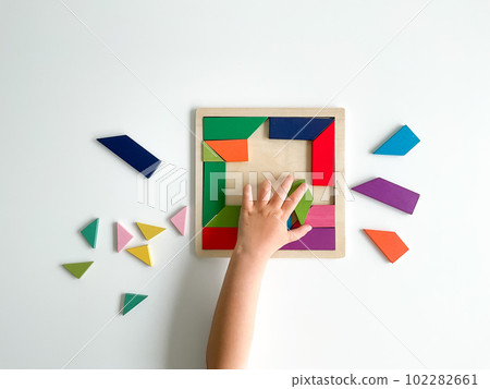 childs hand collects multicolored wooden mosaic on white background. 102282661