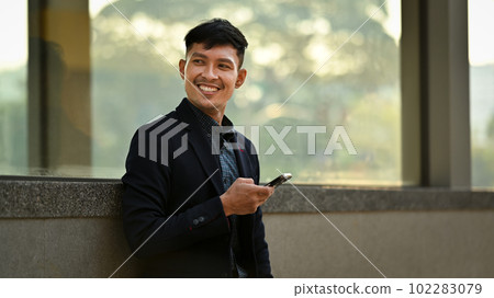 Portrait of businessman using mobile phone while sitting on bench outdoor. People, communication, technology 102283079