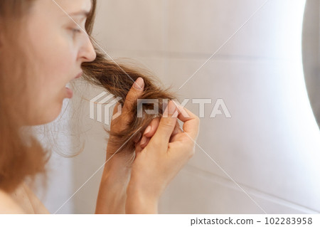 Closeup profile portrait of upset astonished woman looking at her dry hair, having problems, needs to change shampoo or special treatment at trichological clinic. Closeup profile portrait of upset astonished woman looking at her dry hair, having problems, needs to change shampoo or special treatment at trichological clinic. 102283958