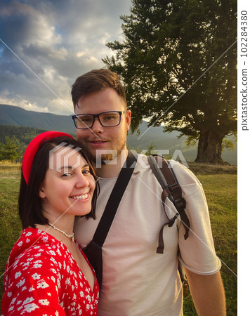 a couple stands under a big old beech tree with a view of the mountains and the sunset a couple stands under a big old beech tree with a view of the mountains and the sunset 102284380