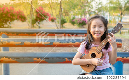 Little asian child girl play the ukulele, in the garden on the Steel pipe 102285394