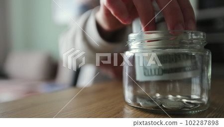 Woman putting a roll of money in a glass jar. Family saving money. Money box. 102287898