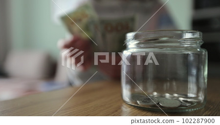 Woman putting a roll of money in a glass jar. Family saving money. Money box. 102287900