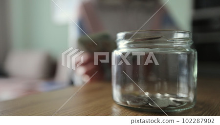 Close up woman takes dollars from the piggy bank. Glass jar with cash. The cash in the piggy bank. 102287902