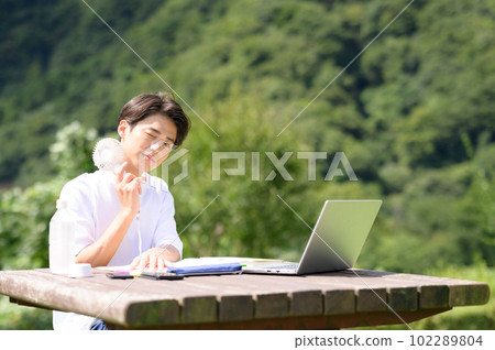 A student studying while using an electric fan outdoors A student studying while using an electric fan outdoors 102289804