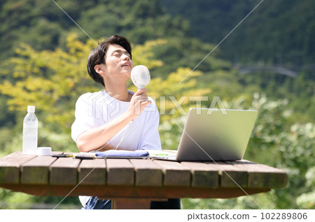A student studying while using an electric fan outdoors 102289806