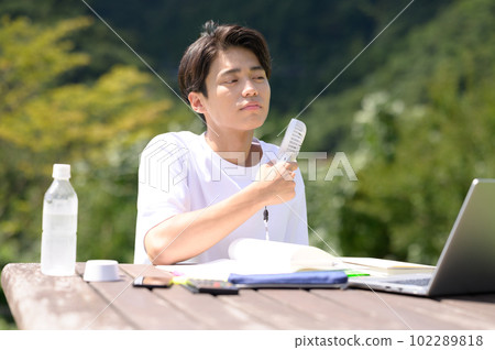A student studying while using an electric fan outdoors 102289818