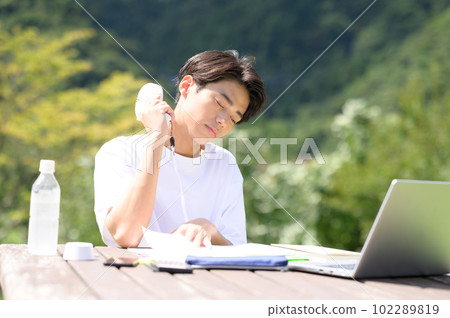 A student studying while using an electric fan outdoors 102289819