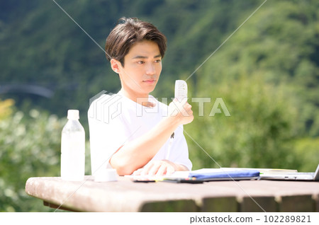 A student studying while using an electric fan outdoors A student studying while using an electric fan outdoors 102289821