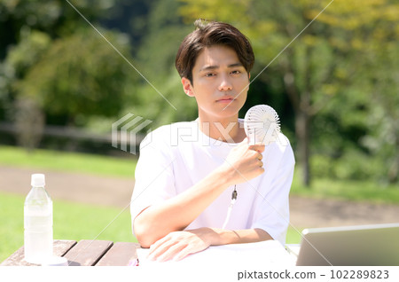 A student studying while using an electric fan outdoors 102289823