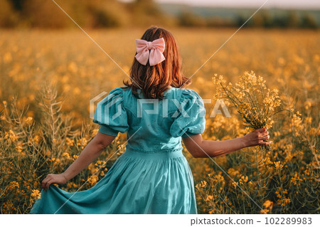 Unrecognizable woman in yellow canola flowers field.Lady in retro dress. Harvest Unrecognizable woman in yellow canola flowers field.Lady in retro dress. Harvest 102289983