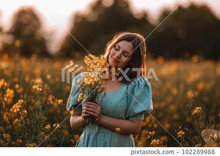 Happy woman in blooming canola flowers field. Lady in retro dress, spring season Happy woman in blooming canola flowers field. Lady in retro dress, spring season 102289988