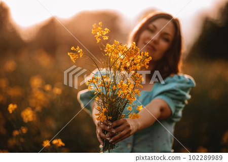 Happy woman in blooming canola flowers field. Lady in retro dress, spring season Happy woman in blooming canola flowers field. Lady in retro dress, spring season 102289989