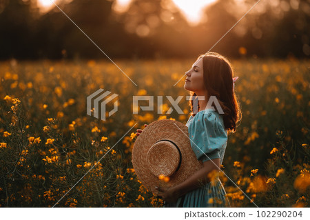 Happy woman in blooming canola flowers field. Lady in retro dress, spring season 102290204