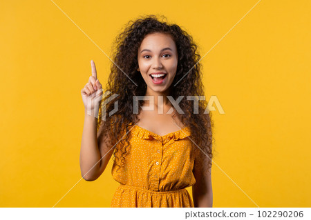 Summer pensive woman having idea eureka moment, pointing finger up on yellow 102290206