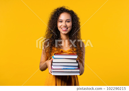 Happy student woman with stack of books from library on yellow background Happy student woman with stack of books from library on yellow background 102290215