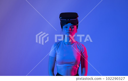 Close up of young woman stands in studio wearing VR glasses and swiping scrolling zooming with hands in a virtual space while interacting with a objects in a metaverse. Virtual reality technology. 102290327
