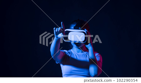 Woman using virtual reality glasses in a studio. Business woman wearing VR goggles and interacts with cyberspace using swipe and stretching gestures. Woman using virtual reality glasses in a studio. Business woman wearing VR goggles and interacts with cyberspace using swipe and stretching gestures. 102290354