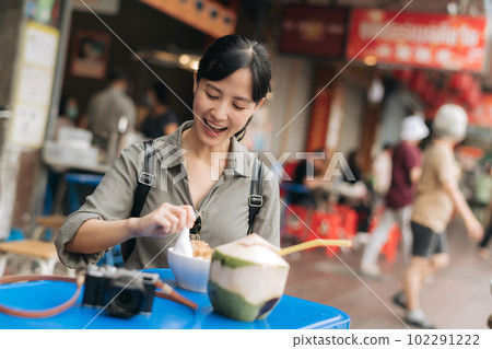 Happy young Asian woman backpack traveler enjoying street food at China town street food market in Bangkok, Thailand. Traveler checking out side streets. 102291222