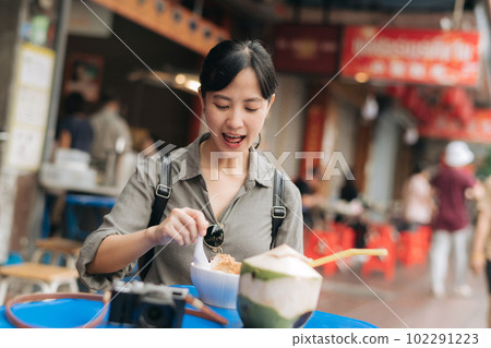 Happy young Asian woman backpack traveler enjoying street food at China town street food market in Bangkok, Thailand. Traveler checking out side streets. Happy young Asian woman backpack traveler enjoying street food at China town street food market in Bangkok, Thailand. Traveler checking out side streets. 102291223