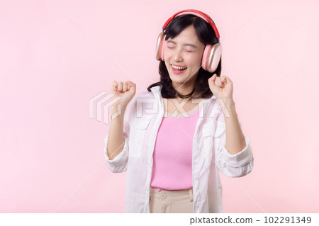Smile pretty asian model person listen music song and enjoy dance with wireless headphone online audio radio sound. Positive fun exited joyful youth female woman on pink isolated background studio 102291349