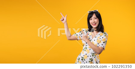 Portrait beautiful young asian woman wearing springtime dress and pointing to copy space for advertising isolated on yellow background. Summertime advertising banner concept. Portrait beautiful young asian woman wearing springtime dress and pointing to copy space for advertising isolated on yellow background. Summertime advertising banner concept. 102291350