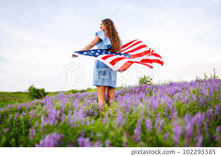 Young woman with american USA flag on blooming meadow. Independence Day, 4th July. Young woman with american USA flag on blooming meadow. Independence Day, 4th July. 102293385