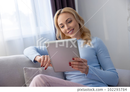 Contented blonde lady reading something on her tablet computer 102293784