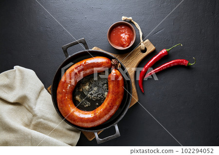 Grilled sausage rolled into a ring in a cast iron pan with pepper and ketchup on a black stone background 102294052
