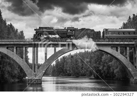 Retro steam train moves above the river. 102294327