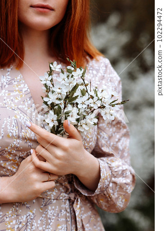 Woman in a dress on a background of white flowers of an apple tree 102294472