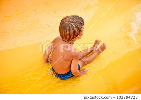 Tanned joyful kid rides on a water slide, amusement attraction in the water park, children's amusement ride roller coaster. 102294728