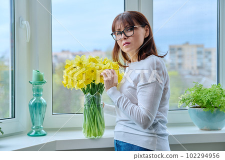 Middle aged woman with bouquet of flowers, near window 102294956