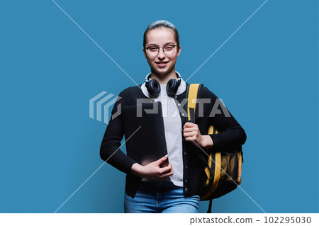 Teenage girl student with backpack holding laptop on blue background 102295030