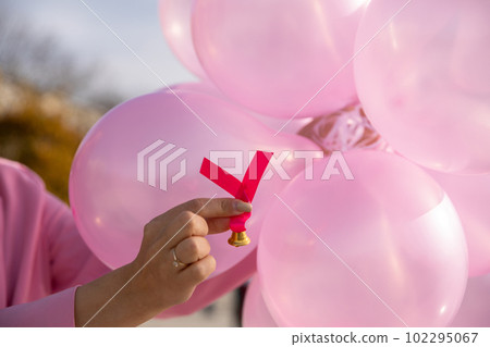In the hand a pink ribbon against a background of pink balloons. Prevention of periodic breast examination. 102295067