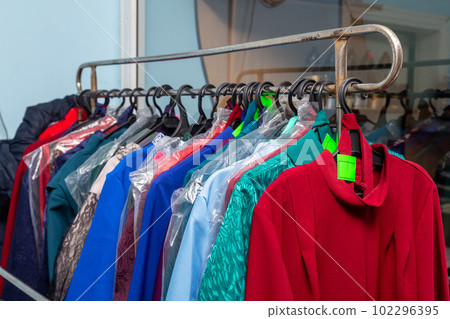 Hangers with men suits and women clothes for the deceased in a funeral goods store. 102296395