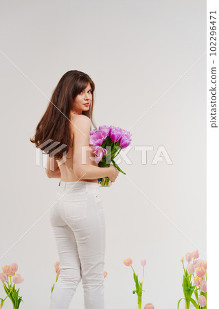 a gentle brunette topless in a room with bouquets of tulips on floor. rear view  102296471