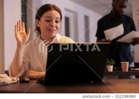 Smiling employee greeting colleague on videocall, discussing startup project, waving hello. Corporate worker answering teleconference call in office with sunset light, remote conversation Smiling employee greeting colleague on videocall, discussing startup project, waving hello. Corporate worker answering teleconference call in office with sunset light, remote conversation 102296960