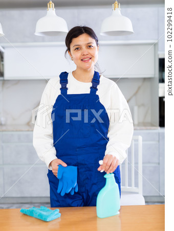 Young smiling cleaning lady standing in home kitchen with detergent 102299418