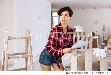 Woman with documents in her hands checks the quality of the completed repairs in cottage room Woman with documents in her hands checks the quality of the completed repairs in cottage room 102299484