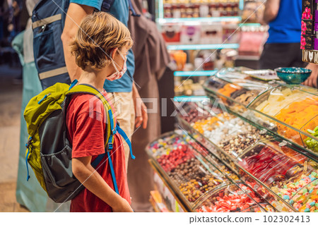 The boy looks at the counter with Turkish sweets. Traditional oriental sweet pastry cookies, nuts, dried fruits, pastilles, marmalade, Turkish desert with sugar, honey and pistachio, in display at a The boy looks at the counter with Turkish sweets. Traditional oriental sweet pastry cookies, nuts, dried fruits, pastilles, marmalade, Turkish desert with sugar, honey and pistachio, in display at a 102302413