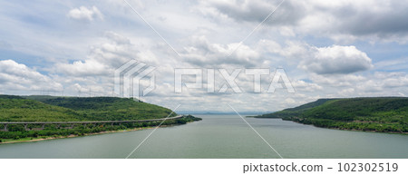 Landscape green mountain with wind turbine farm and water reservoir with blue sky and white clouds. Wind energy. Wind power. Sustainable, renewable energy. Green technology. Sustainable development. 102302519