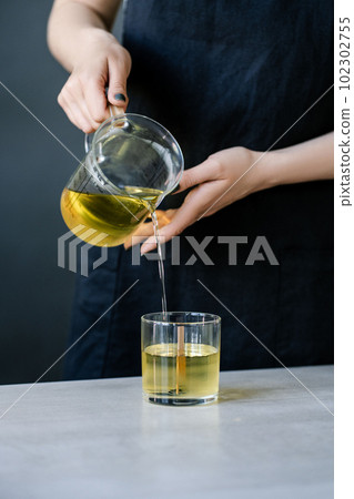 The girl pours wax into glass glasses with wicks. The girl pours wax into glass glasses with wicks. 102302755