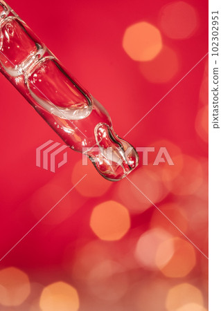 Pipette with serum on a red holiday background with bokeh. Pipette with serum on a red holiday background with bokeh. 102302951