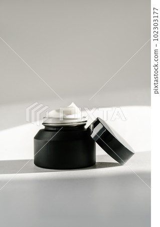 Black cosmetic bottle on a background flooded with sunlight. 102303177