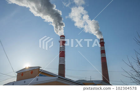 Smoke from industrial pipes against blue sky with bright sun close up. Industrial zone. Environmental pollution. Horizontal format. 102304578