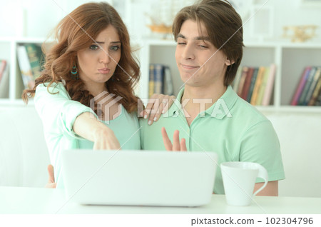 Portrait of surprised young couple pointing at laptop at home 102304796